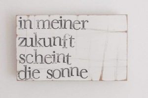 Ein weißes Holzschild mit deutscher Schrift in schwarzen Buchstaben lautet: In meiner zukunft scheint die sonne.