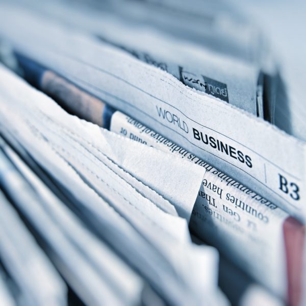 Nahaufnahme eines Zeitungsstapels, wobei die oberste Zeitung die Rubrik "World Business" in fetten Buchstaben zeigt. Die Seiten sind leicht aufgefächert, so dass Schlagzeilen und Textspalten sichtbar werden.
