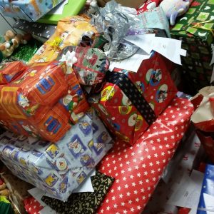 Ein großer Stapel eingepackter Geschenke in verschiedenen bunten und festlichen Geschenkpapieren mit Geschenkanhängern, die auf Tischen übereinander gestapelt sind, bereit zum Verteilen.