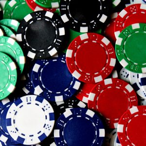 Ein Stapel bunter Pokerchips in den Farben Rot, Grün, Blau, Schwarz und Weiß, die verstreut und überlappend angeordnet sind und üblicherweise in Kasinospielen wie Poker und Blackjack verwendet werden.