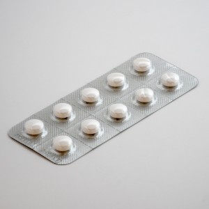 Eine silberne Blisterpackung mit zehn runden weißen Tabletten wird auf eine glatte, hellgraue Fläche gelegt.