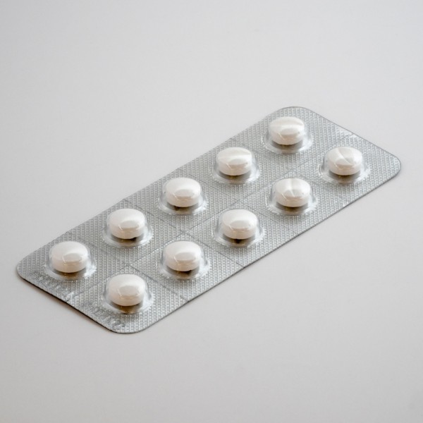 Eine silberne Blisterpackung mit zehn runden weißen Tabletten wird auf eine glatte, hellgraue Fläche gelegt.