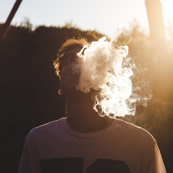 Eine Person, die ein Hemd mit der Nummer 78 trägt, atmet eine Dampfwolke aus, die ihr Gesicht teilweise verdeckt, während im Hintergrund die Sonne scheint und Bäume zu sehen sind.