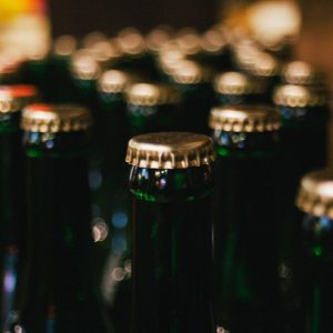 Nahaufnahme mehrerer grüner Glasflaschen mit Metallkappen, die dicht nebeneinander in Reihen angeordnet sind. Der Fokus liegt auf den Oberseiten der Flaschen, der Hintergrund ist unscharf.