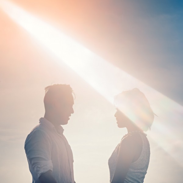 Ein Mann und eine Frau stehen sich unter einem hellen Himmel gegenüber, der von einem dramatischen Sonnenstrahl und Streulicht beleuchtet wird und eine romantische und verträumte Atmosphäre schafft.