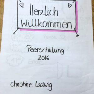 Auf einem handgeschriebenen Schild auf weißem Papier steht: Herzlich willkommen, Peerschulung 2016, und Christine Ludwig, mit kleinen Herzchen und einem rosa Rand um den oberen Text.
