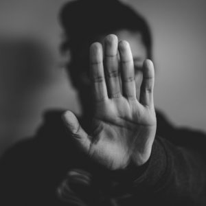Eine Person hält ihre Hand mit der Handfläche in Richtung der Kamera, so dass ihr Gesicht verdeckt ist. Das Bild ist in Schwarz-Weiß und der Hintergrund ist unscharf.