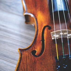 Nahaufnahme einer Geige mit Schwerpunkt auf den Saiten, dem Steg und dem F-Loch, mit einer Holzoberfläche im Hintergrund. Die Beleuchtung hebt die Holzmaserung und den Glanz des Instruments hervor.