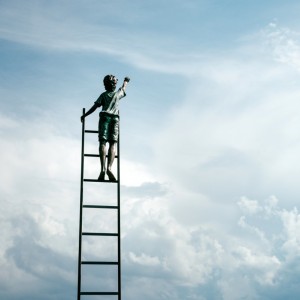Ein Kind steht auf einer hohen Leiter, streckt einen Arm nach oben und hält ein Fernglas in der Hand, vor einem hellen, bewölkten Himmel.
