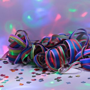 Bunte Luftschlangen und Konfetti, die auf einer weißen Fläche verstreut sind, mit leuchtenden blauen, roten und grünen Lichtreflexen, die eine festliche Atmosphäre auf der Hintergrundwand schaffen.