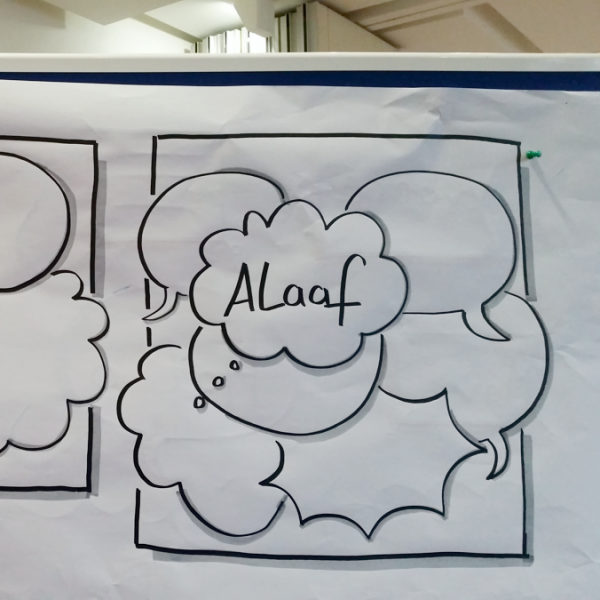 Ein Whiteboard zeigt handgezeichnete Comic-Tafeln mit Sprech- und Gedankenblasen. Die linke Tafel zeigt verschiedene sich überschneidende Formen und ein Papier mit Linien, während die rechte Tafel das Wort Alaaf in einer wolkenförmigen Blase zeigt.