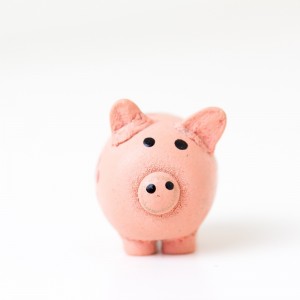 Ein rosafarbenes Sparschwein aus Keramik steht auf einer weißen Fläche mit einfarbigem weißem Hintergrund und blickt nach vorne. Das Sparschwein hat eine runde Nase, schwarze Augen und kleine Ohren.