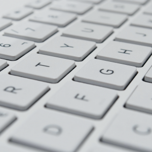 Nahaufnahme einer weißen Computertastatur, die die Oberseiten der quadratischen Tasten mit schwarzen Buchstaben und Zahlen zeigt, darunter die Buchstaben E, R, T, Y, U, G, H sowie die Zahlen 5, 6 und 7.