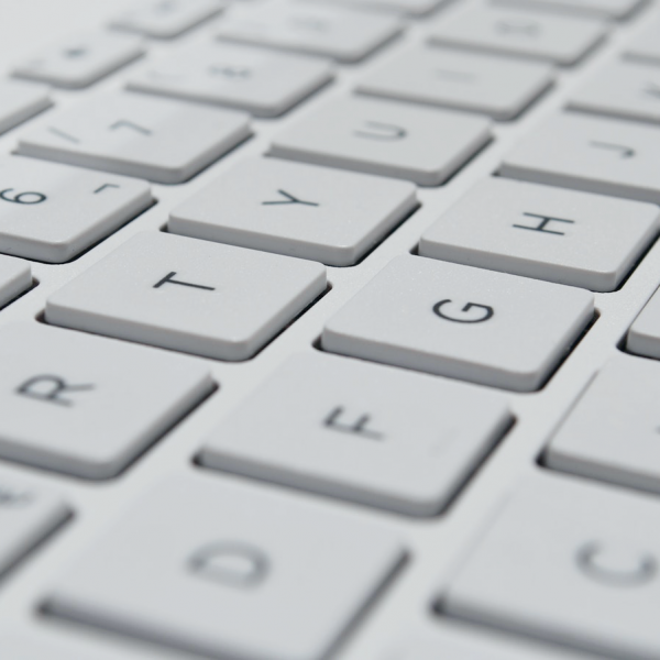 Nahaufnahme einer weißen Computertastatur, die die Oberseiten der quadratischen Tasten mit schwarzen Buchstaben und Zahlen zeigt, darunter die Buchstaben E, R, T, Y, U, G, H sowie die Zahlen 5, 6 und 7.
