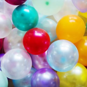 Eine Nahaufnahme von bunten Luftballons, darunter rote, gelbe, grüne, blaue, violette und weiße, die sich gegenseitig überlappen und den gesamten Rahmen ausfüllen, wodurch eine festliche und fröhliche Atmosphäre entsteht.