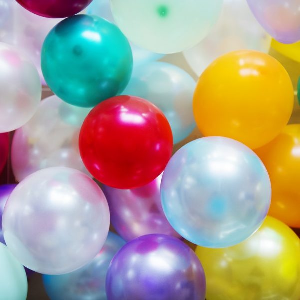 Eine Nahaufnahme von bunten Luftballons, darunter rote, gelbe, grüne, blaue, violette und weiße, die sich gegenseitig überlappen und den gesamten Rahmen ausfüllen, wodurch eine festliche und fröhliche Atmosphäre entsteht.