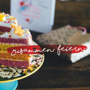 Ein bunter Schichtkuchen mit Sterndekoration und Streuseln steht auf einem Tortenständer mit Blumen; ein Stück ist herausgeschnitten. Im Hintergrund sind ein Geschenk und eine Karte zu sehen. Der Text lautet "zusammen feiern" auf Deutsch.