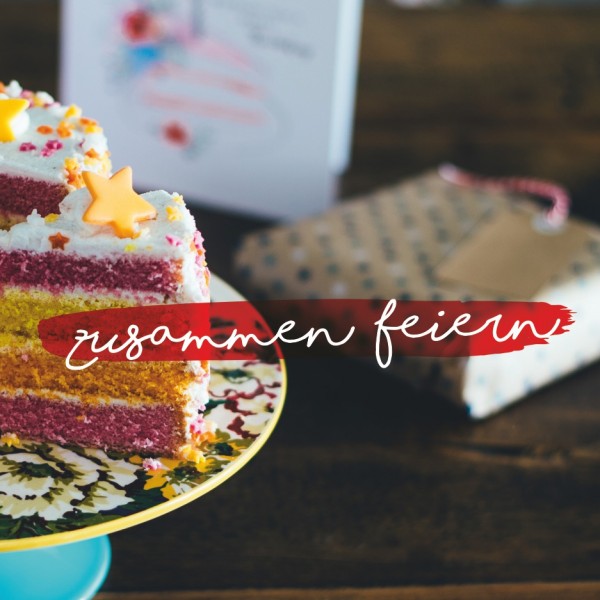 Ein bunter Schichtkuchen mit Sterndekoration und Streuseln steht auf einem Tortenständer mit Blumen; ein Stück ist herausgeschnitten. Im Hintergrund sind ein Geschenk und eine Karte zu sehen. Der Text lautet "zusammen feiern" auf Deutsch.