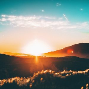 Sonnenaufgang über sanften Hügeln mit hellem Sonnenlicht, das den Himmel erhellt, einen goldenen Schimmer auf die Landschaft wirft und eine heitere Atmosphäre schafft.