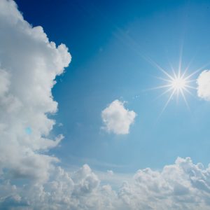 Strahlender Sonnenschein vor einem klaren blauen Himmel mit vereinzelten weißen Schäfchenwolken, die eine ruhige und friedliche Atmosphäre schaffen.
