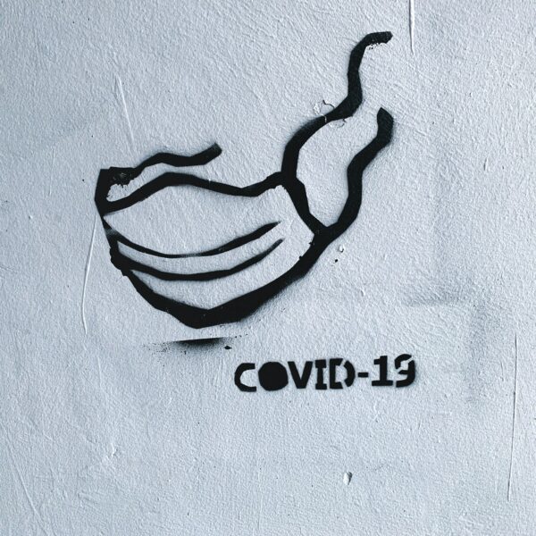 Schwarzes Schablonengraffiti einer Gesichtsmaske und des Textes COVID-19 auf einer rauen weißen Wand, das die Coronavirus-Pandemie und das Maskentragen symbolisiert.