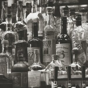 Ein Schwarz-Weiß-Foto, das ein überfülltes Regal mit verschiedenen Spirituosenflaschen zeigt, darunter Whiskey, Gin und Bourbon, die dicht nebeneinander angeordnet sind, mit sichtbaren Etiketten und unterschiedlichen Flaschenformen.