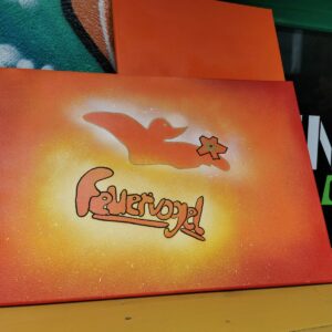Auf einer Leinwand mit orange-gelbem Farbverlauf ist die Silhouette eines Vogels mit einer sternförmigen Blume zu sehen, darunter steht in stilisierten, graffitiartigen Buchstaben das Wort Feuervogel.