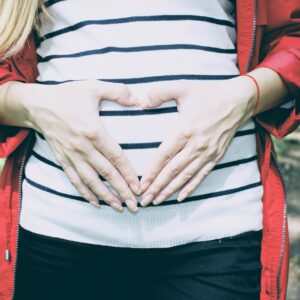Eine Frau, die mit ihren Händen auf dem Bauch ein Herz bildet.