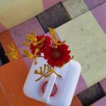 Ein kleiner weißer Plastikbehälter enthält rote und gelbe Blumen, die auf einer bunten, gestreiften Holzfläche mit orangen, gelben, rosa und grünen Brettern stehen.