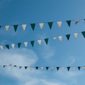 Drei Reihen von abwechselnd grünen und weißen dreieckigen Wimpelflaggen hängen über einem klaren blauen Himmel, an dem im Hintergrund ein paar Wolkenfetzen zu sehen sind.