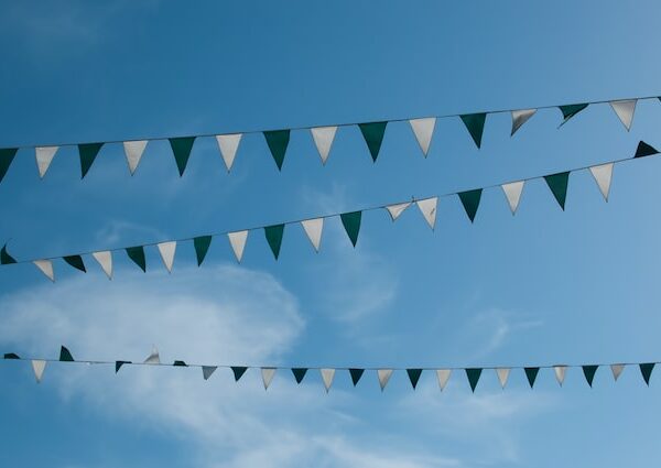 Drei Reihen von abwechselnd grünen und weißen dreieckigen Wimpelflaggen hängen über einem klaren blauen Himmel, an dem im Hintergrund ein paar Wolkenfetzen zu sehen sind.