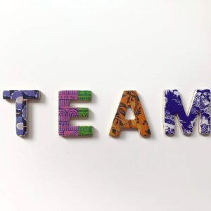 Vier bunte Buchstaben auf weißem Hintergrund, die TEAM buchstabieren; jeder Buchstabe hat ein anderes Muster und eine andere Farbe: blau, grün, orange und lila mit verschiedenen Mustern.