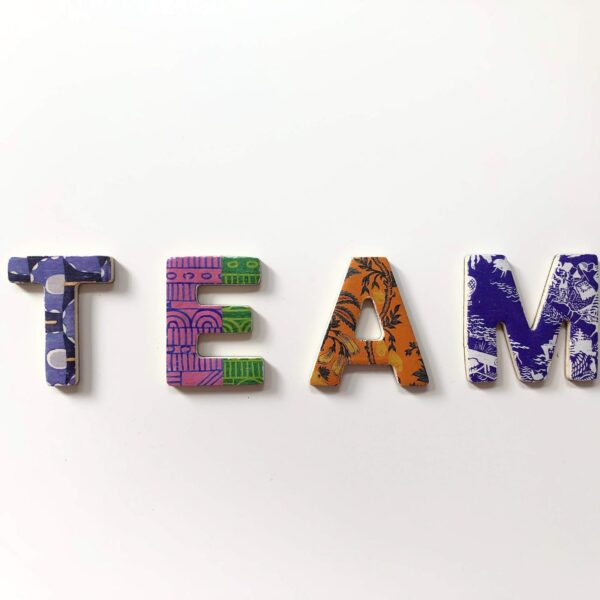 Vier bunte Buchstaben auf weißem Hintergrund, die TEAM buchstabieren; jeder Buchstabe hat ein anderes Muster und eine andere Farbe: blau, grün, orange und lila mit verschiedenen Mustern.
