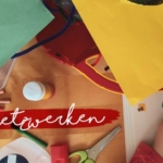 Kinderhände malen mit Buntstiften auf einem unübersichtlichen Tisch mit Papier, Buntstiften und Kunstzubehör. Das Wort "Netwerken" steht in weißer Schrift auf einem rot gemalten Streifen quer über dem Bild.