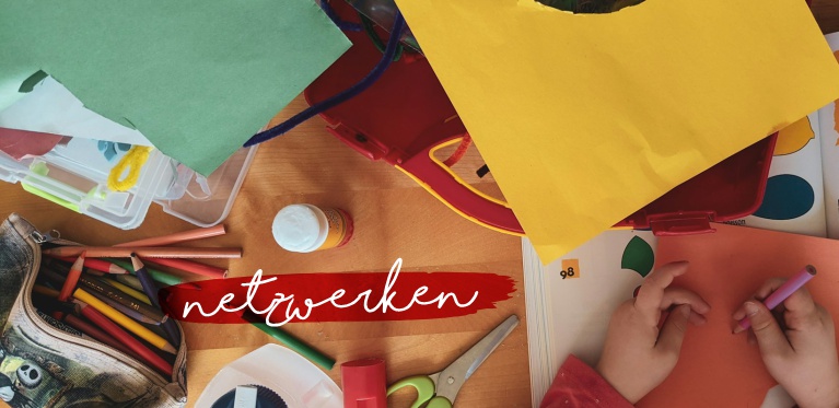 Kinderhände malen mit Buntstiften auf einem unübersichtlichen Tisch mit Papier, Buntstiften und Kunstzubehör. Das Wort "Netwerken" steht in weißer Schrift auf einem rot gemalten Streifen quer über dem Bild.