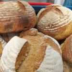 Mehrere runde, rustikale Brotlaibe mit goldbrauner Kruste und mehlbestäubten Mustern sind in einer blauen Kiste aufeinander gestapelt.