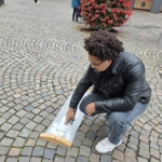 Unser Praktikant Noah sprüht den Link abgezockt.de mit einer Schablone und Kreidefarbe auf den Boden.